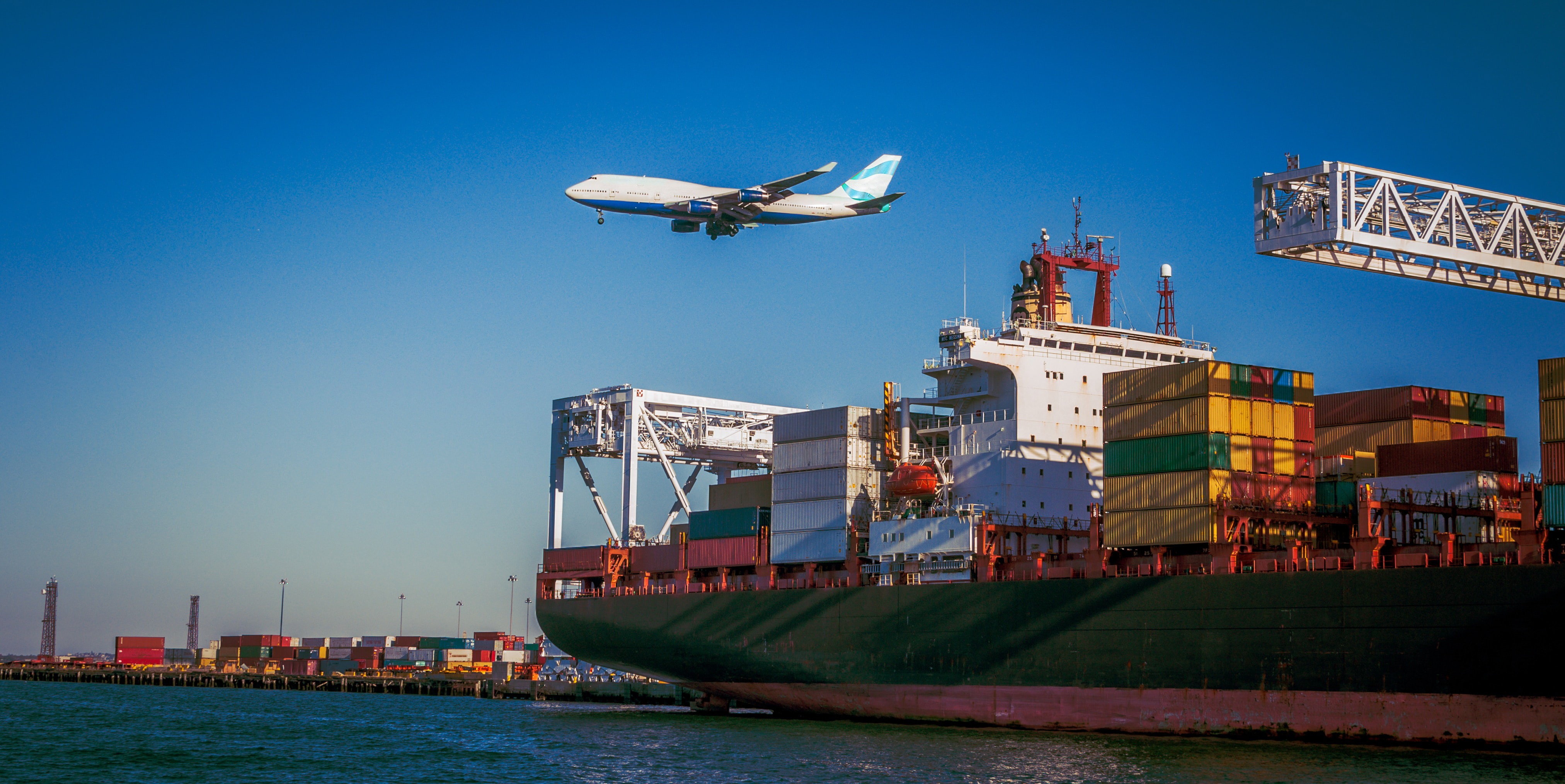 Photo showing a container ship at the port and an airplane in the sky